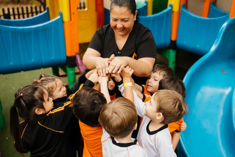 Educadora com os alunos da Educação Infantil de mãos juntas no parquinho